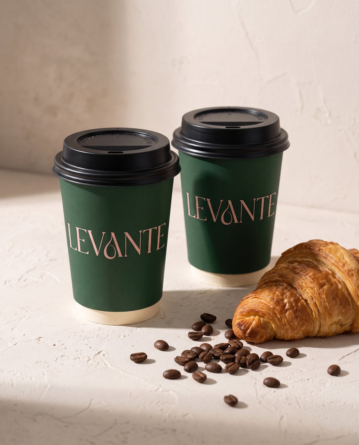 Two Levante hot cups in green with a croissant and coffee beans